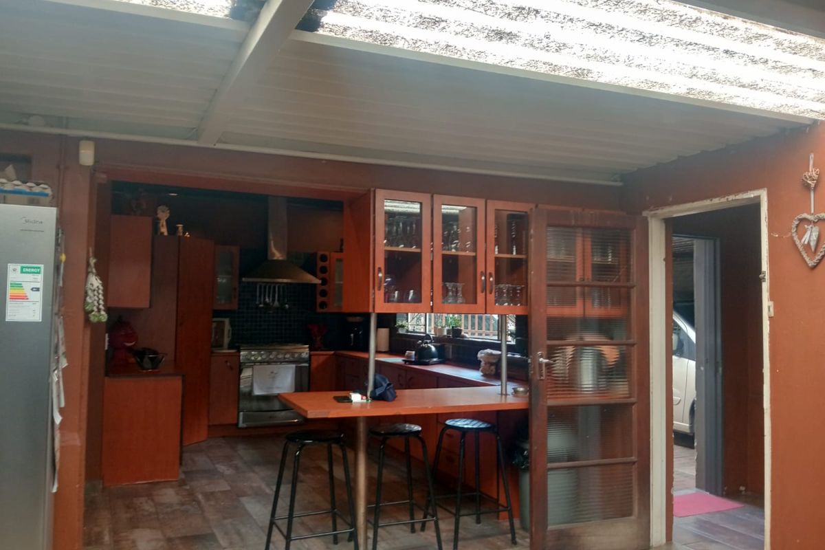 A functional kitchen featuring built-in wooden cabinetry, a stainless steel extractor fan, gas stove, and a breakfast bar, set under a translucent roof structure.