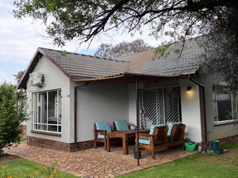 Rear view of the house featuring a paved patio area, tiled roof, and established garden surroundings.