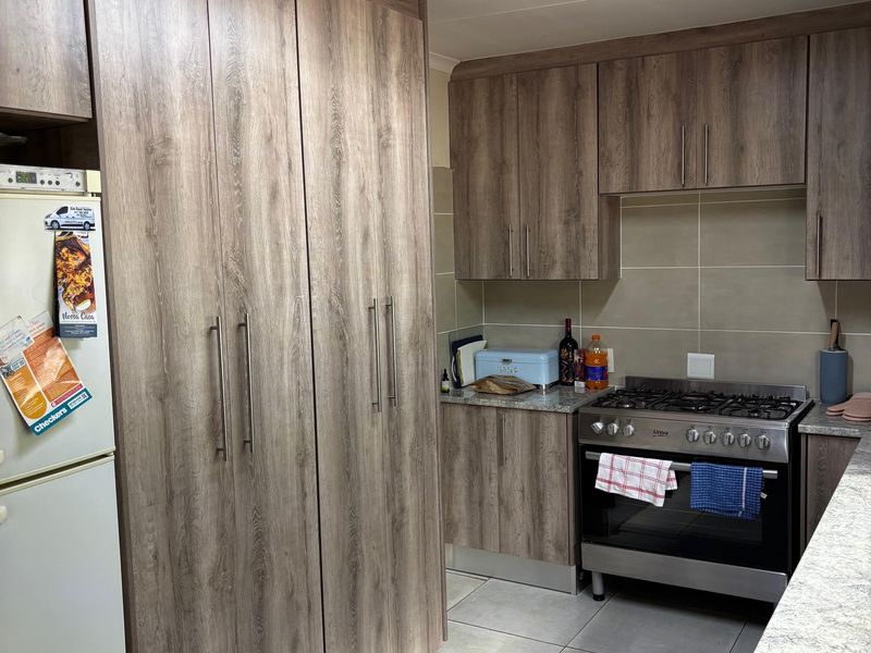 A functional kitchen featuring wood-look cabinetry, granite countertops, a gas stove with oven, and neutral tiled flooring.