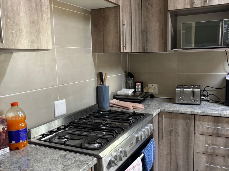 A functional kitchen featuring wood-look laminate cabinetry, granite countertops, a gas stove, and a built-in microwave with neutral tiled backsplash.