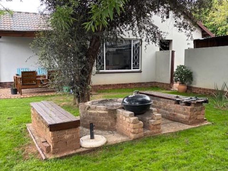 Rear garden area featuring a built-in brick braai with integrated seating benches, paved patio space, and established lawn.