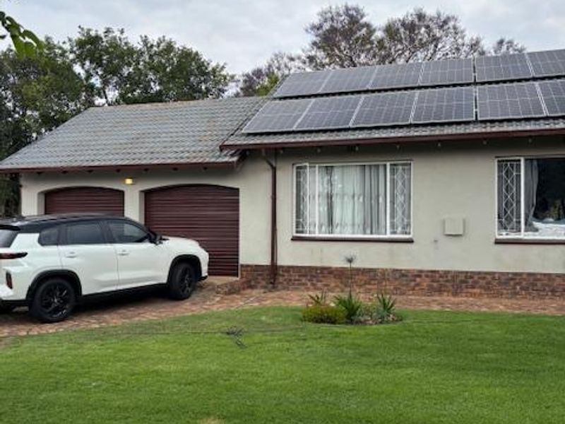 Front elevation of a house featuring a paved driveway, double garage, and roof-mounted solar panels set against a well-maintained lawn.