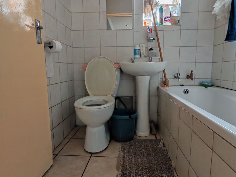 A functional bathroom featuring a pedestal basin, toilet, and bathtub with tiled finishes, requiring cosmetic updates to improve its overall condition and aesthetic appeal.