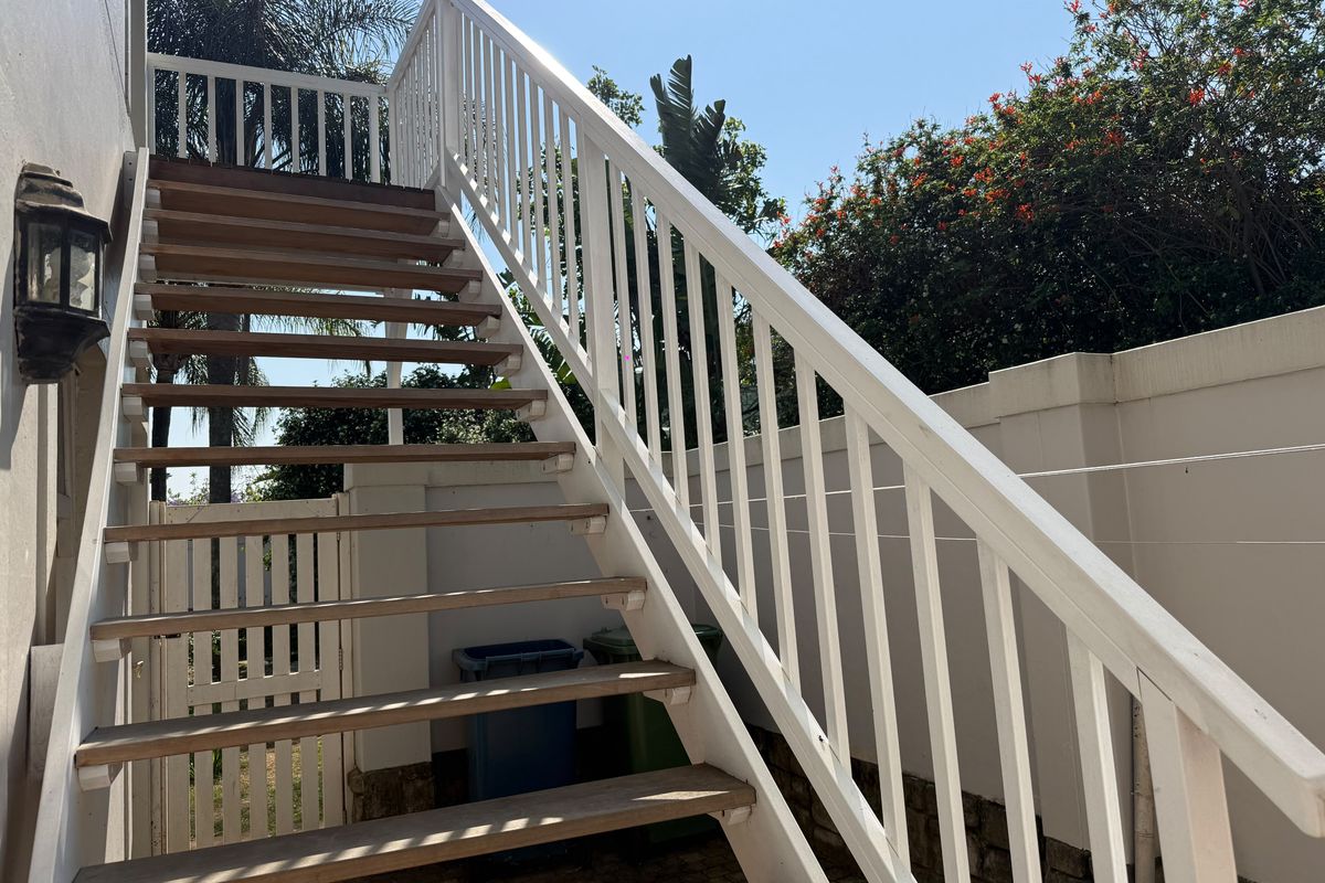 Exterior view of a timber staircase leading to an upper level, featuring a painted balustrade and adjacent boundary wall.