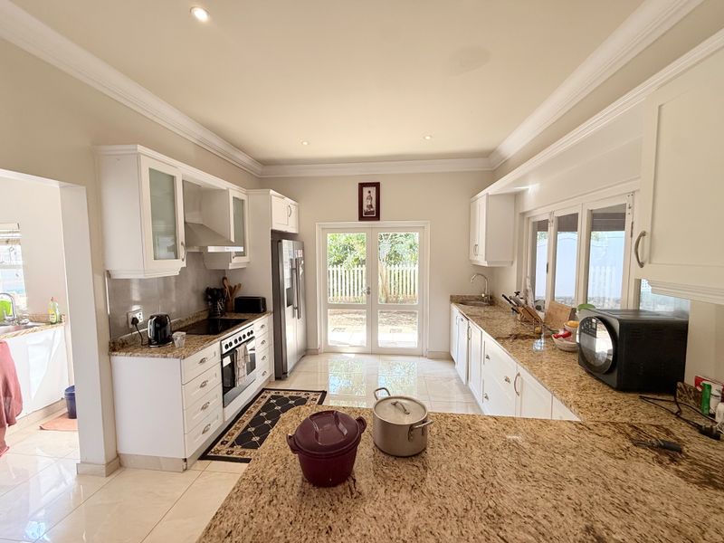 A well-lit kitchen featuring granite countertops, white cabinetry, built-in appliances, and direct access to the garden through double glass doors.