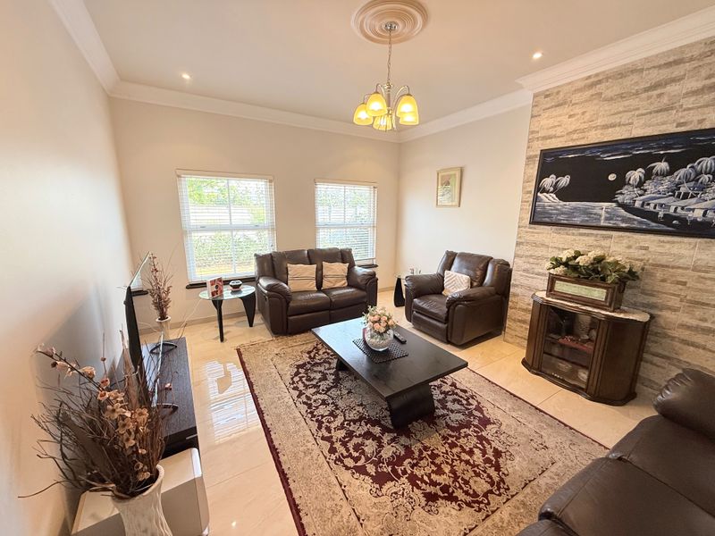 A well-maintained living room featuring a stone-clad feature wall, tiled flooring, recessed lighting, and elegant crown molding.