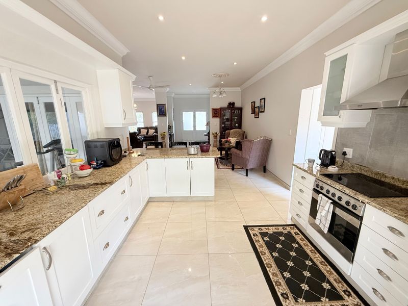 Spacious open-plan kitchen and living area featuring granite countertops, modern cabinetry, built-in appliances, and bright tiled flooring throughout.