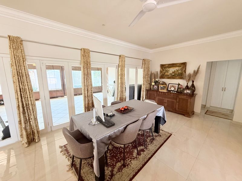 Spacious dining room featuring tiled flooring, crown molding, a ceiling fan, and large sliding glass doors providing access to the patio area.