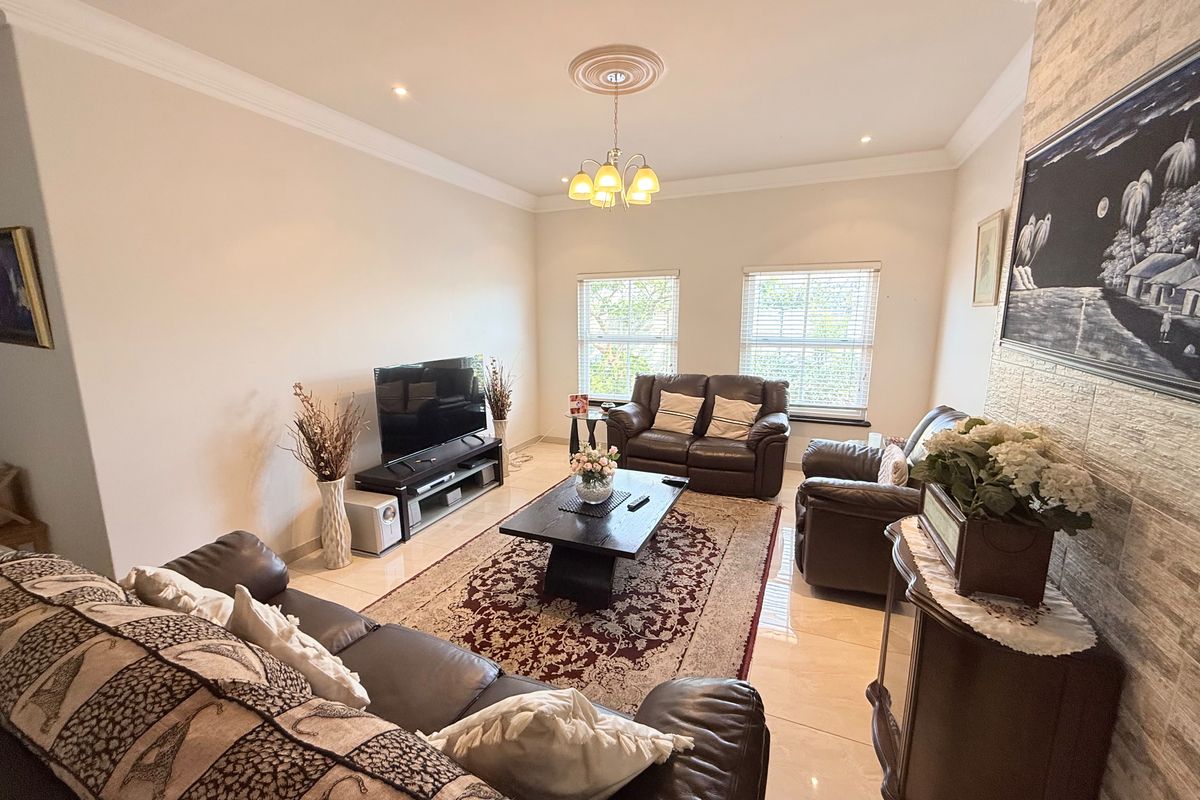 Spacious living room featuring polished tiled flooring, a decorative ceiling rose, and a textured stone feature wall, creating a comfortable and inviting atmosphere.