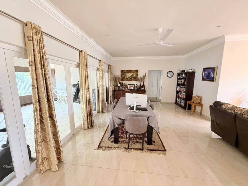 Spacious open-plan living and dining area featuring large glass french doors, polished tile flooring, and elegant crown molding throughout.