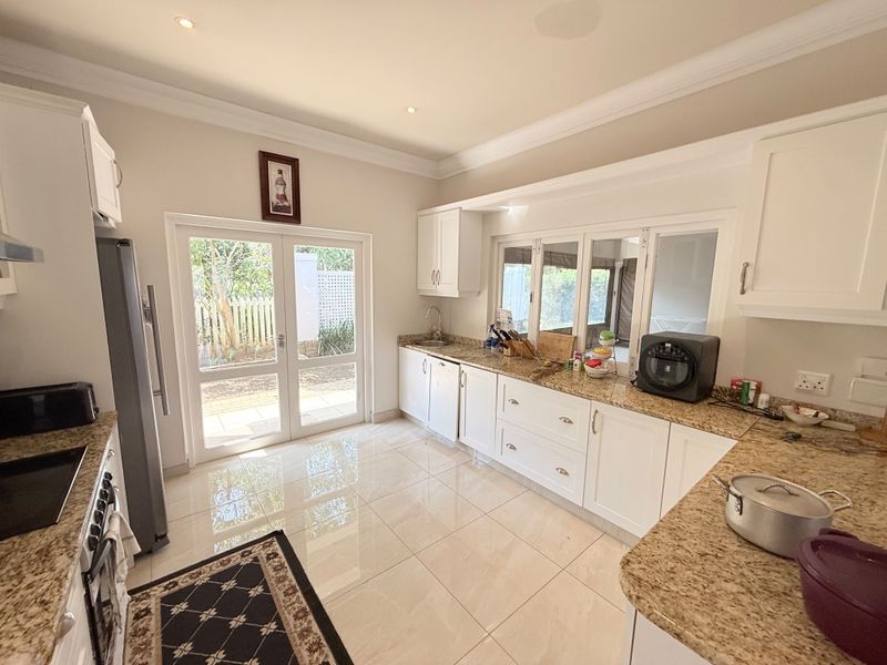 A bright, well-maintained kitchen featuring granite countertops, white cabinetry, tiled flooring, and direct access to the outdoor area through glass doors.