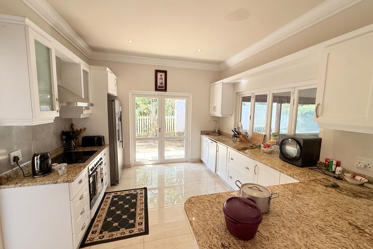 Spacious kitchen featuring granite countertops, ample white cabinetry, built-in appliances, and direct access to the garden through glass french doors.