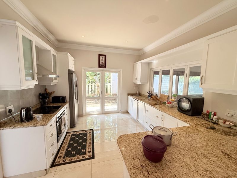 Spacious kitchen featuring granite countertops, ample white cabinetry, built-in appliances, and direct access to the garden through glass french doors.