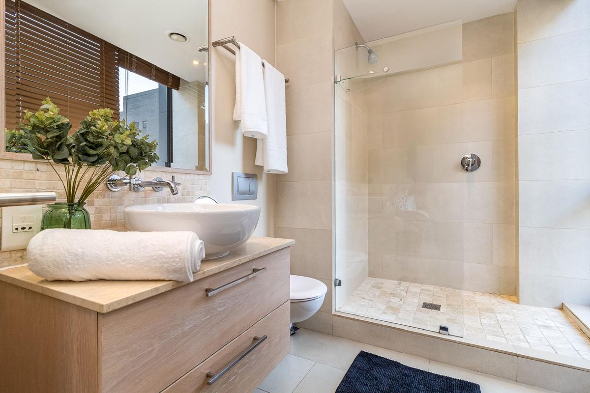 Modern bathroom featuring a wood-finish vanity with a vessel sink, wall-mounted faucet, and a spacious walk-in shower with a glass enclosure.