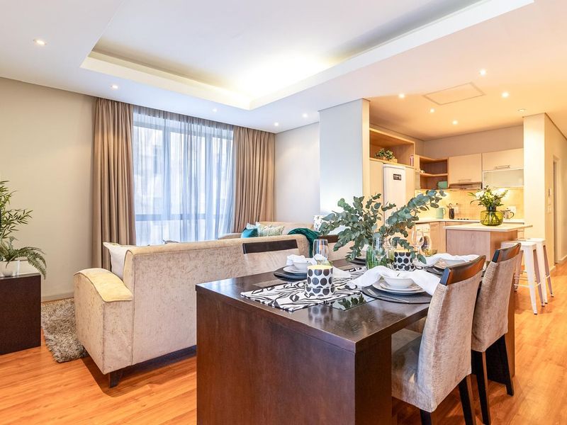 Modern open-plan living and dining area featuring a contemporary kitchen with an island, recessed ceiling lighting, and warm laminate flooring throughout.