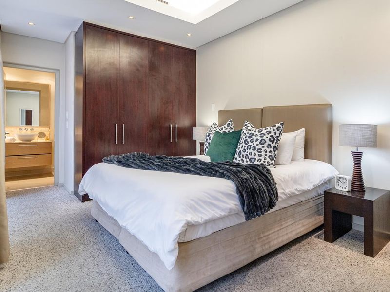 A well-maintained bedroom featuring dark wood built-in cupboards, recessed ceiling lighting, and carpeted flooring, with direct access to an en-suite bathroom.