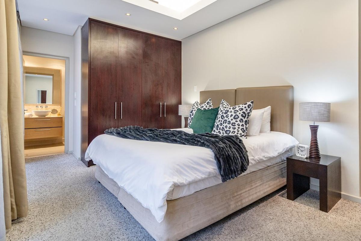 A well-maintained bedroom featuring dark wood built-in cupboards, recessed ceiling lighting, and carpeted flooring, with direct access to an en-suite bathroom.