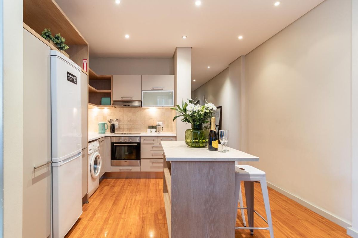 Modern kitchen featuring built-in cabinetry, integrated oven, hob, extractor fan, and a central island, finished with laminate flooring and recessed lighting.