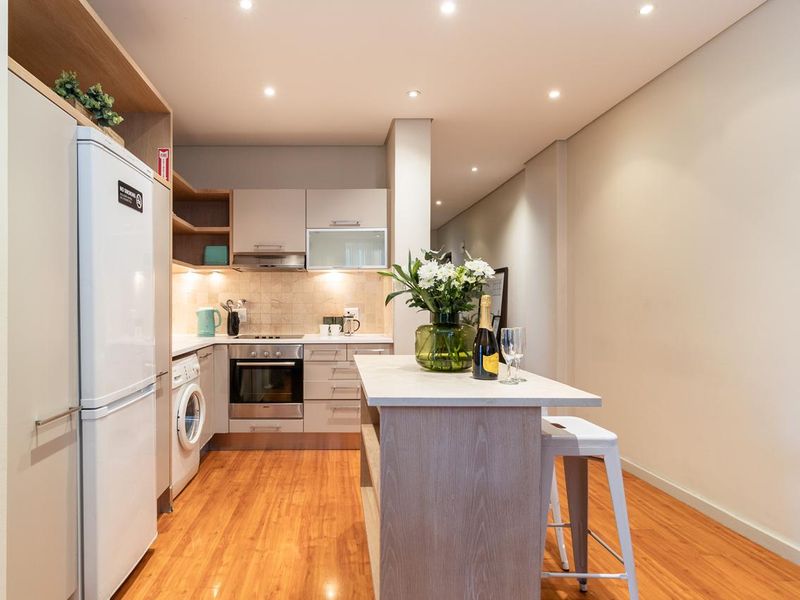 Modern kitchen featuring built-in cabinetry, integrated oven, hob, extractor fan, and a central island, finished with laminate flooring and recessed lighting.