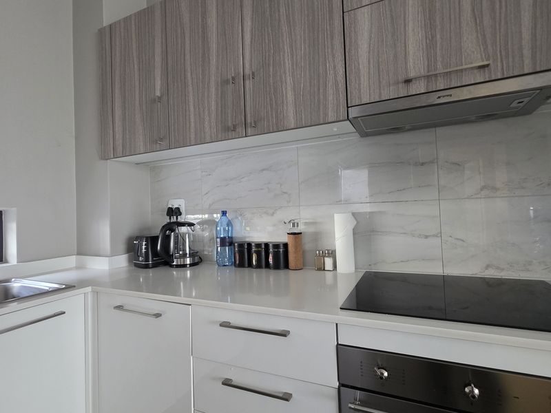 Modern kitchen featuring sleek white lower cabinets, wood-grain upper cabinetry, marble-look backsplash, and integrated stainless steel appliances.