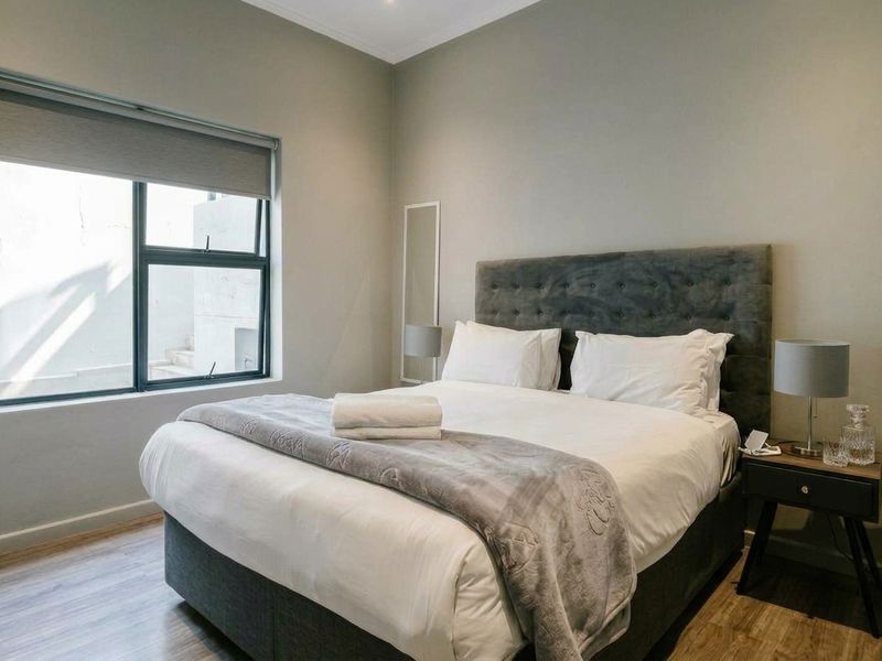 A well-maintained bedroom featuring modern laminate flooring, neutral wall finishes, and an aluminium-framed window with a fitted roller blind.