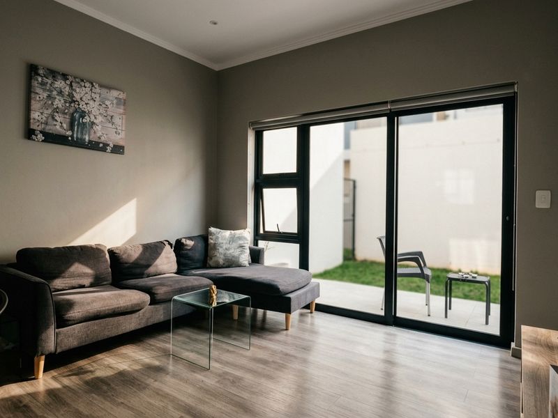 A well-lit living room featuring modern laminate flooring and large sliding glass doors that provide direct access to an outdoor patio area.