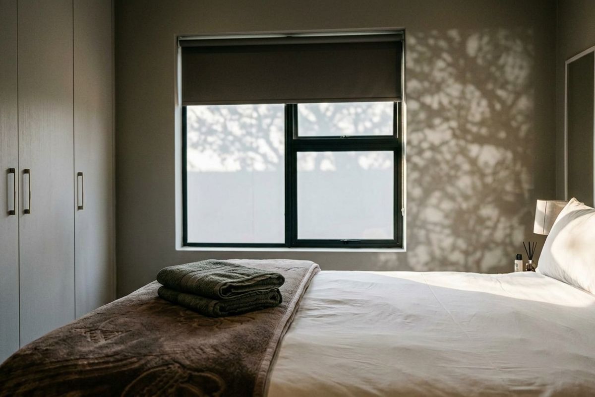 A well-maintained bedroom featuring built-in cupboards, a modern aluminium window frame, and a roller blind, creating a calm and inviting atmosphere.