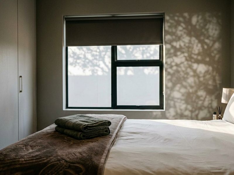 A well-maintained bedroom featuring built-in cupboards, a modern aluminium window frame, and a roller blind, creating a calm and inviting atmosphere.