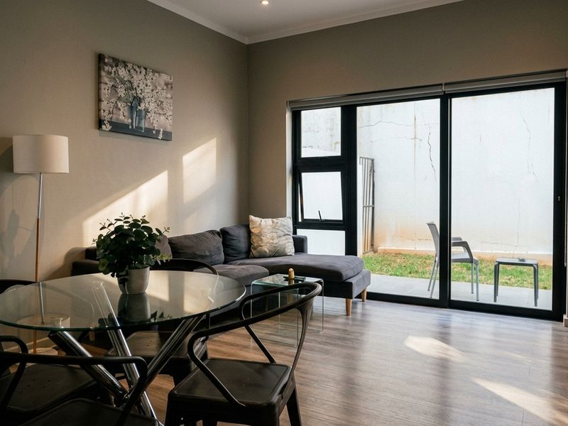 Open-plan living area featuring modern laminate flooring, recessed lighting, and large sliding glass doors providing direct access to a private patio and garden.