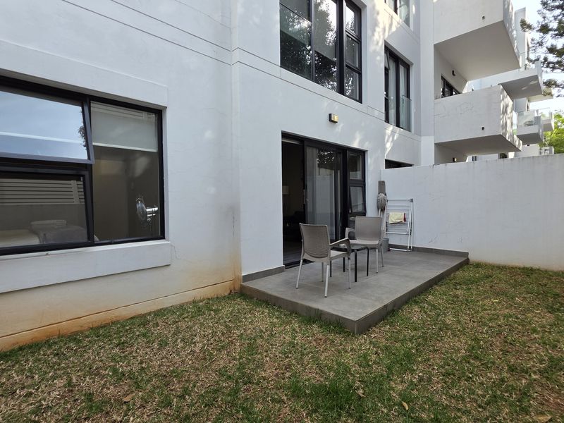 Rear exterior view of the apartment featuring a private tiled patio, sliding glass doors, and a small garden area with boundary wall.