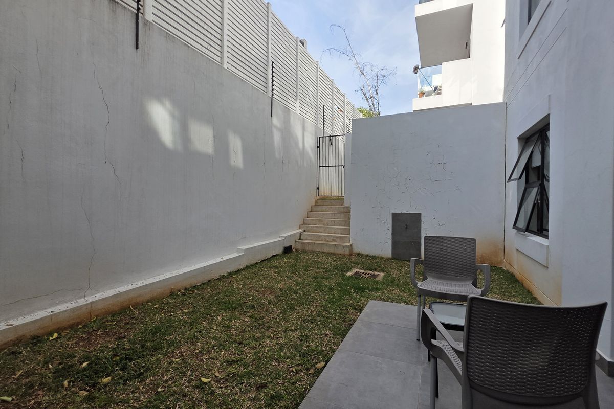 A private rear courtyard featuring a small lawn, paved patio area, and high boundary walls with integrated electric fencing.
