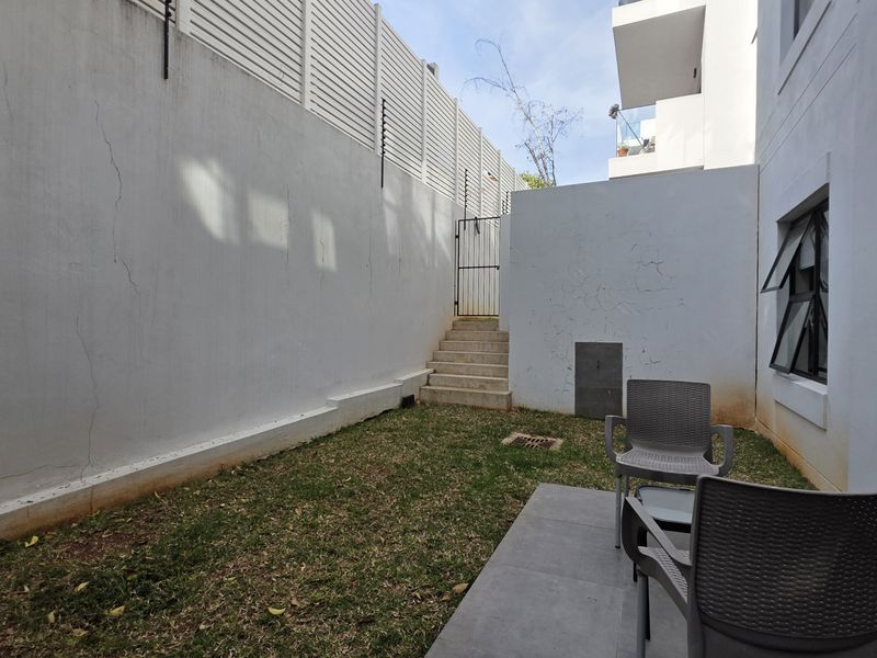 A private rear courtyard featuring a small lawn, paved patio area, and high boundary walls with integrated electric fencing.
