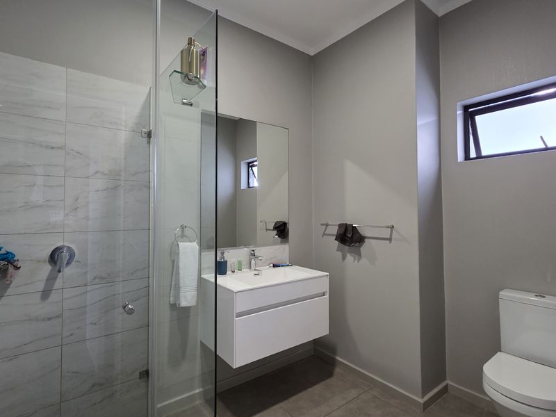 Modern bathroom featuring a walk-in shower with marble-look tiling, a wall-mounted vanity, and a contemporary toilet.