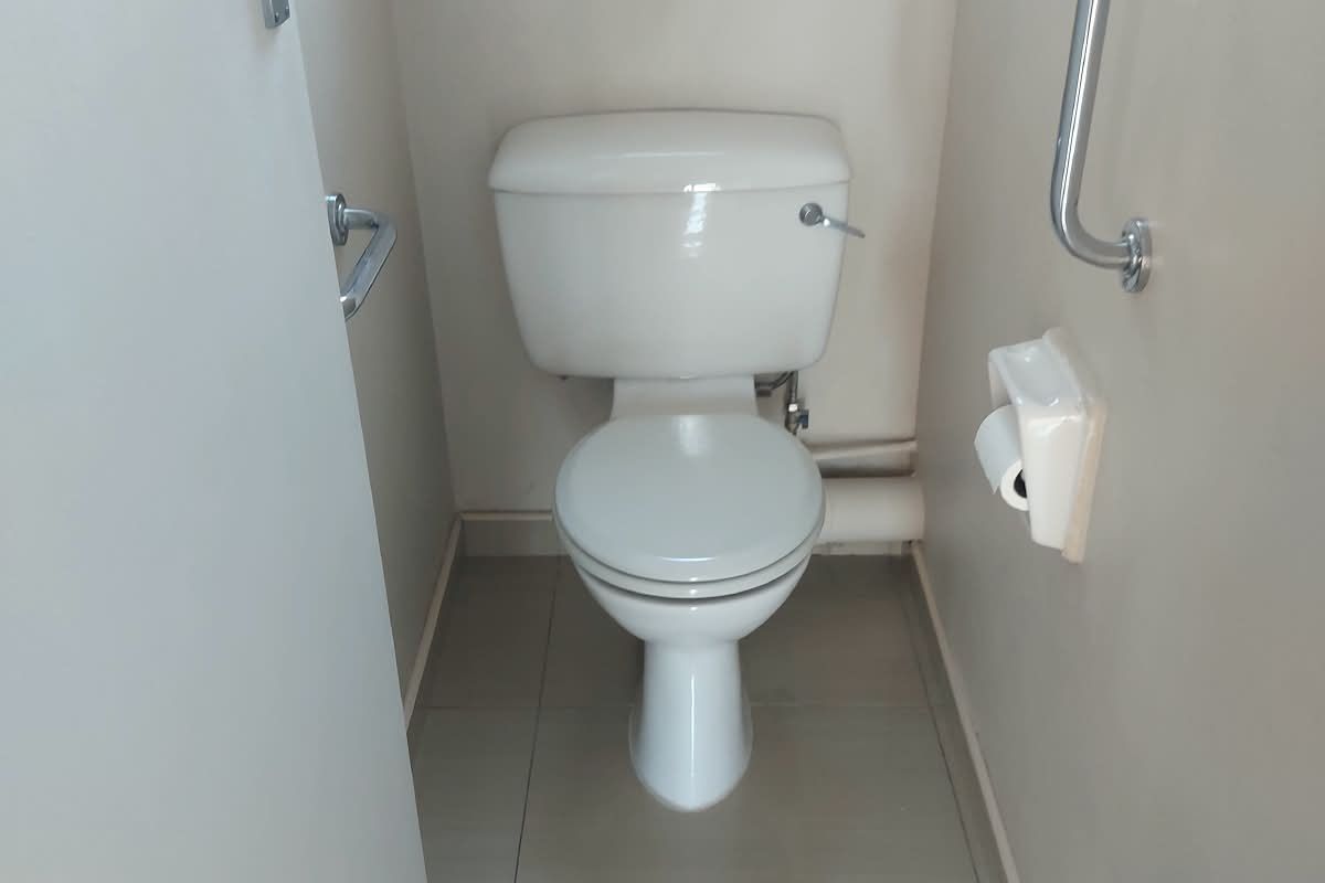 A functional bathroom featuring a standard toilet, tiled flooring, and a wall-mounted grab rail for accessibility.