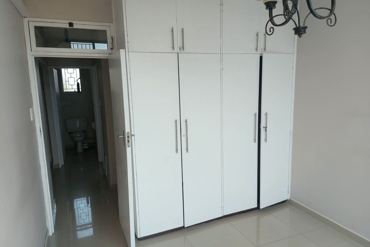 A bedroom featuring built-in cupboards with white cabinetry and tiled flooring, with an adjacent view into a bathroom.