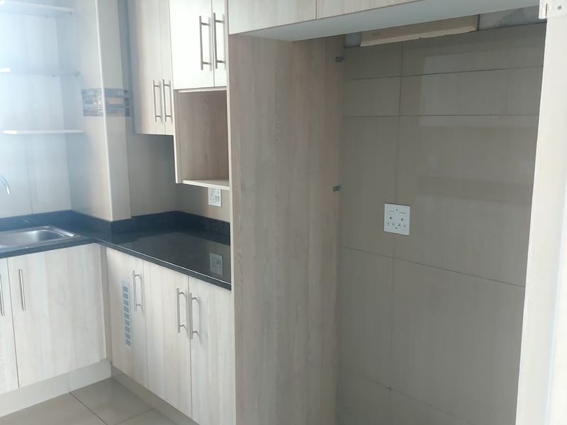 A clean, modern kitchen featuring light wood-finish cabinetry, dark granite countertops, tiled backsplash, and a dedicated space for a refrigerator.