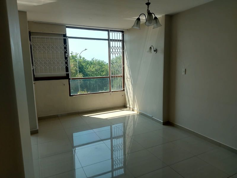 A bright and spacious living area featuring polished tiled flooring, large windows with security bars, and integrated lighting fixtures.