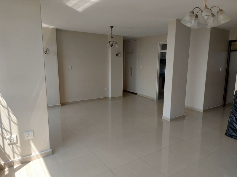 Spacious, light-filled living area featuring neutral tiled flooring, built-in storage cupboards, and multiple lighting fixtures, offering a clean and versatile blank canvas.