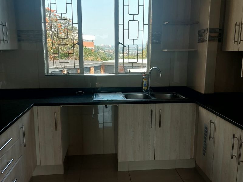 A clean, functional kitchen featuring light wood-finish cabinetry, dark granite countertops, and a double basin sink with a view through the window.
