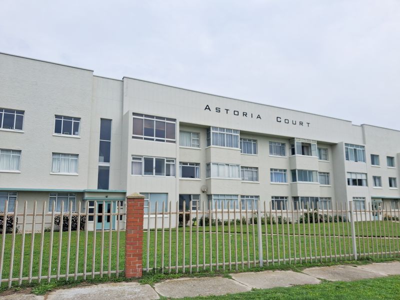 Front elevation of Astoria Court apartment building featuring a multi-story facade with metal security fencing and established lawn area.