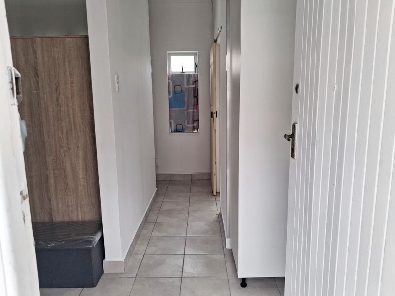 A functional hallway featuring neutral tiled flooring, built-in storage cabinetry, and a small window providing natural light.
