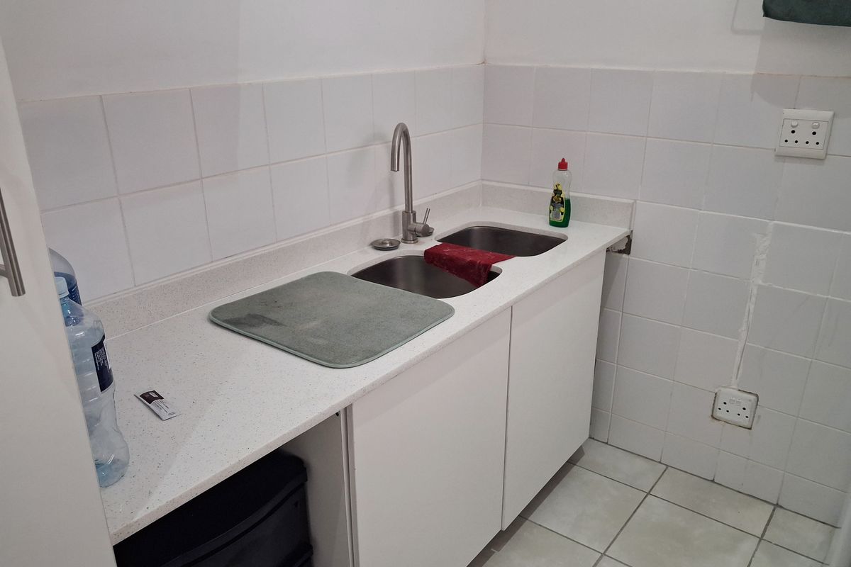 A functional scullery or utility area featuring a stainless steel double sink, white cabinetry, stone-look countertop, and tiled splashback.