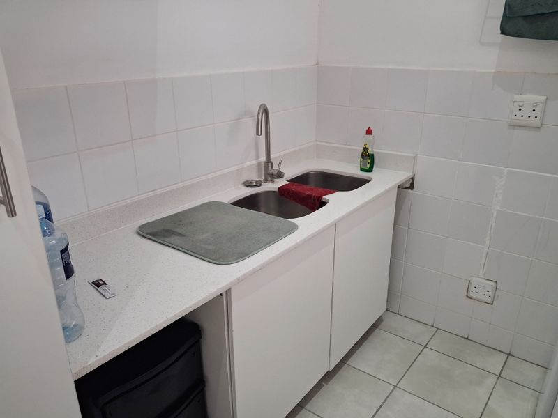 A functional scullery or utility area featuring a stainless steel double sink, white cabinetry, stone-look countertop, and tiled splashback.