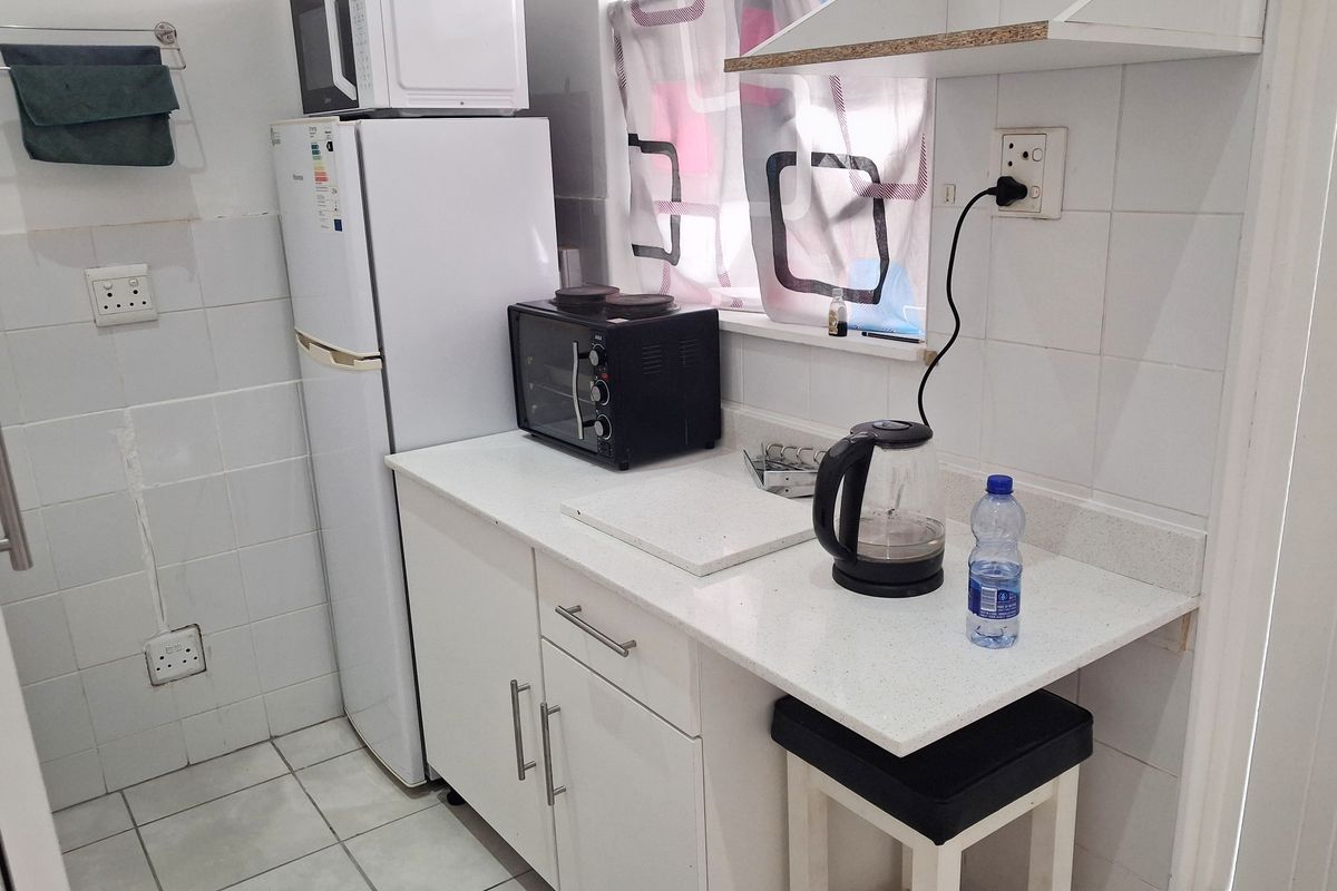 Compact kitchen area featuring white cabinetry, stone countertops, and tiled splashbacks, providing a functional prep space within the apartment.