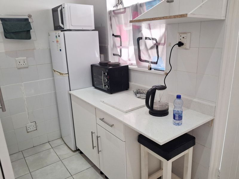 Compact kitchen area featuring white cabinetry, stone countertops, and tiled splashbacks, providing a functional prep space within the apartment.