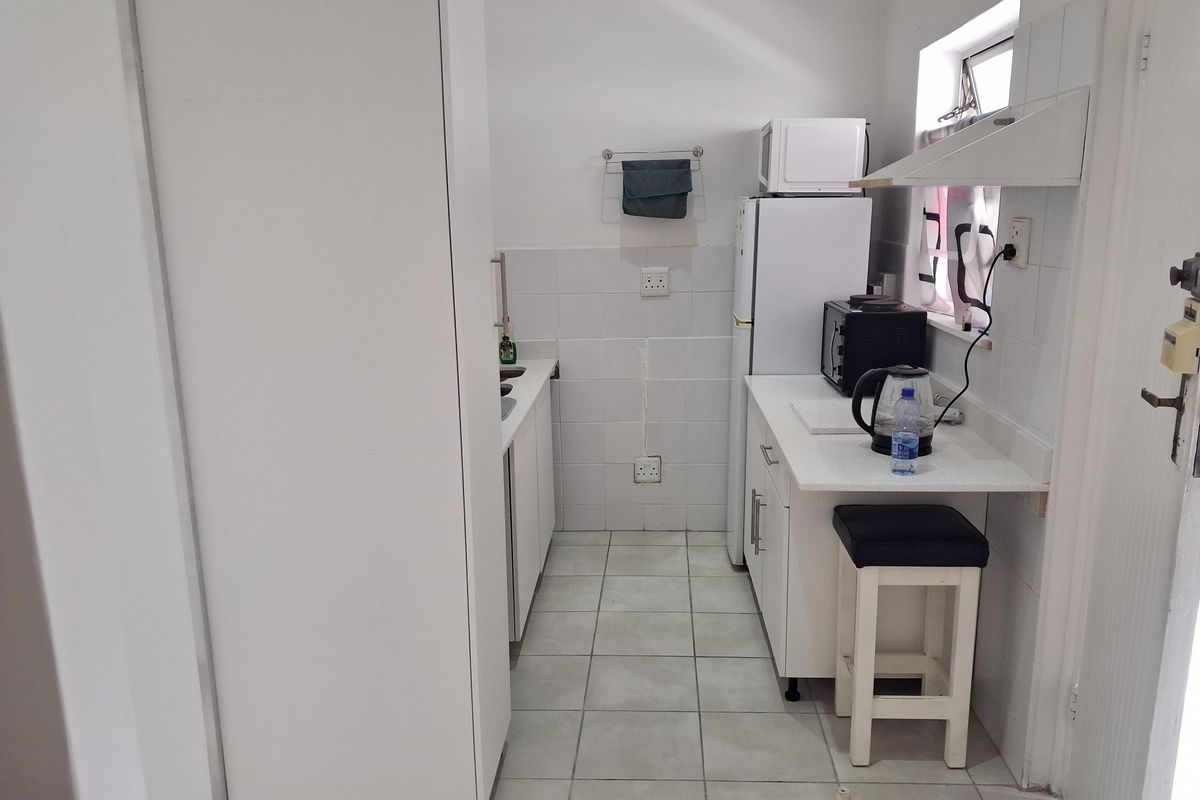 Compact kitchen featuring white cabinetry, tiled splashbacks, and tiled flooring, providing a functional and clean workspace.