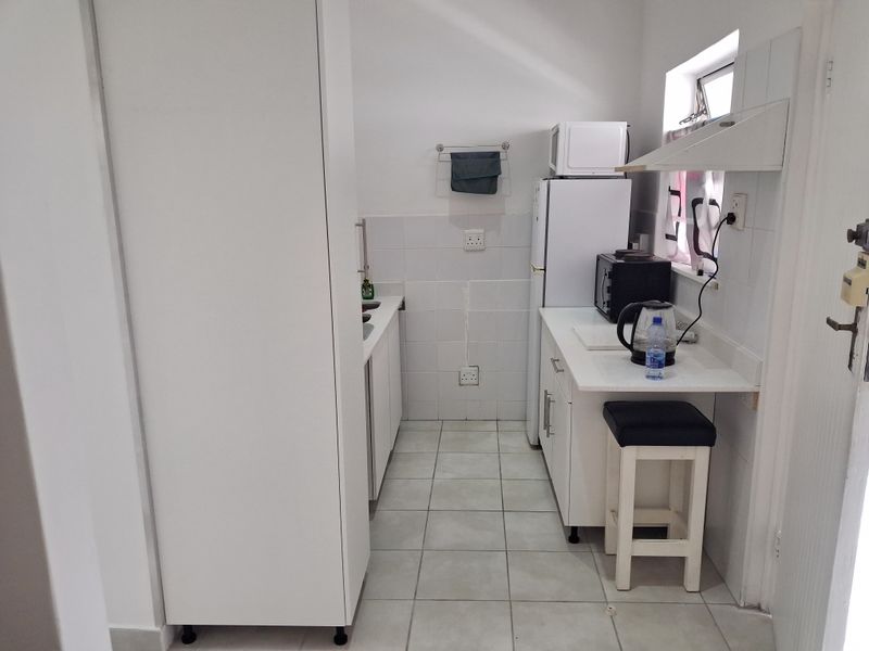 Compact kitchen featuring white cabinetry, tiled splashbacks, and tiled flooring, providing a functional and clean workspace.