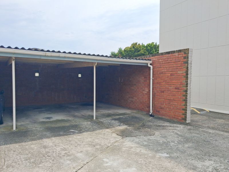 An open-sided carport structure featuring brick walls and a concrete floor, providing covered parking space for the apartment complex.