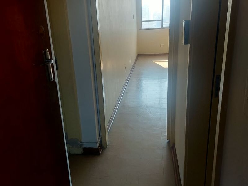 A vacant hallway with vinyl flooring leading towards a sunlit room, showing signs of wear and requiring cosmetic updates.