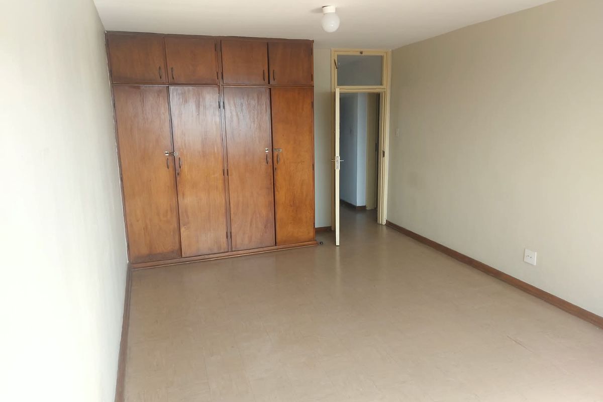 An empty bedroom featuring built-in wooden cupboards with overhead storage and neutral wall finishes, offering a blank canvas for potential updates.